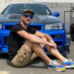 Victor Diakov assis devant une Nissan Skyline R34 GT-R bleue en train de recalculer ses mauvais choix de vie de 2013.