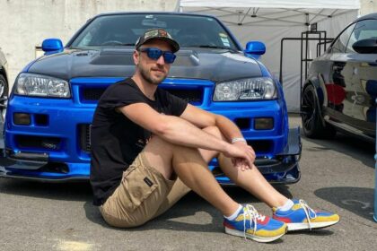 Victor Diakov assis devant une Nissan Skyline R34 GT-R bleue en train de recalculer ses mauvais choix de vie de 2013.