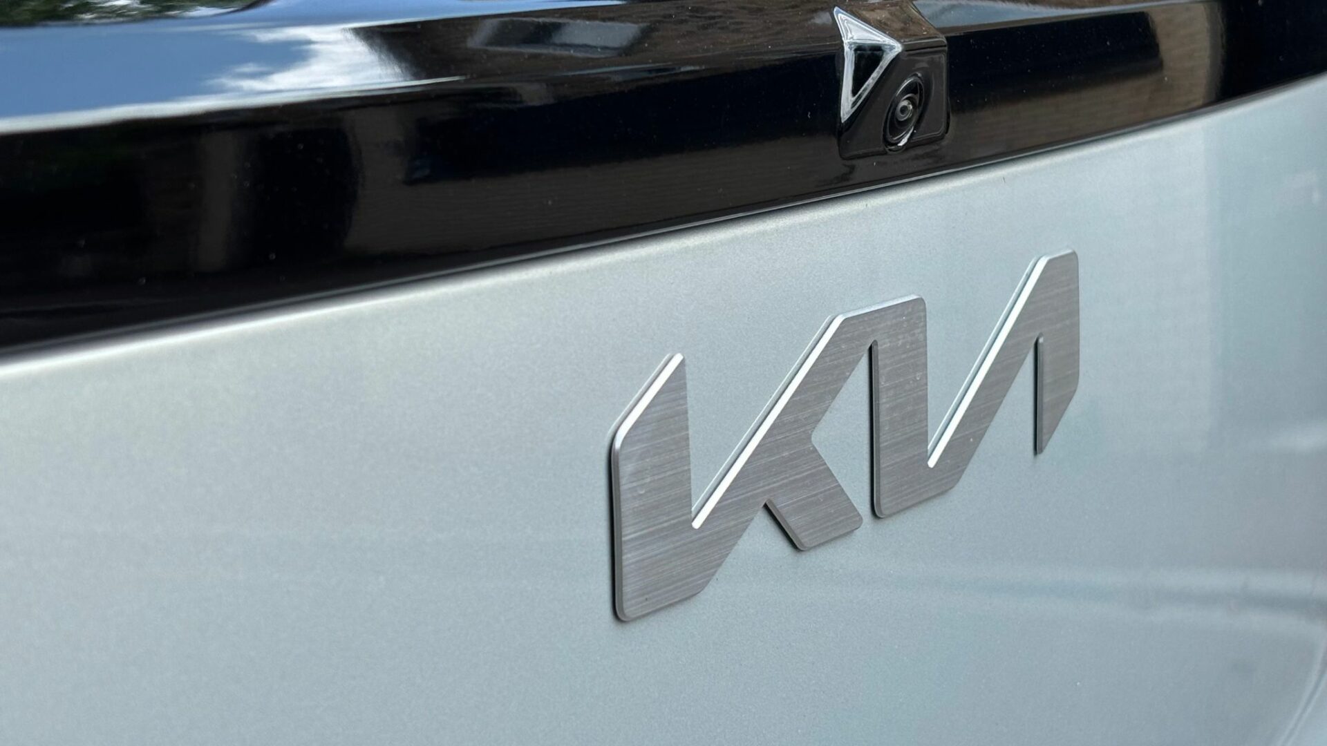 Gros plan sur le logo Kia en aluminium brossé et la caméra de recul intégrée au hayon du Kia Niro Hybride 2026