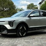 Kia Niro Hybride 2026 gris clair métallique de trois-quarts avant garé sur des pavés avec ses nouveaux phares verticaux