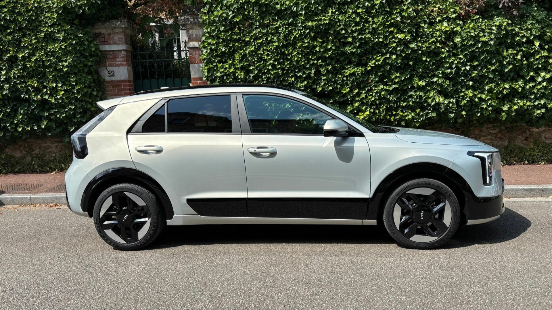Profil du Kia Niro Hybride 2026 en teinte Gris Ivoire stationné devant un mur de lierre