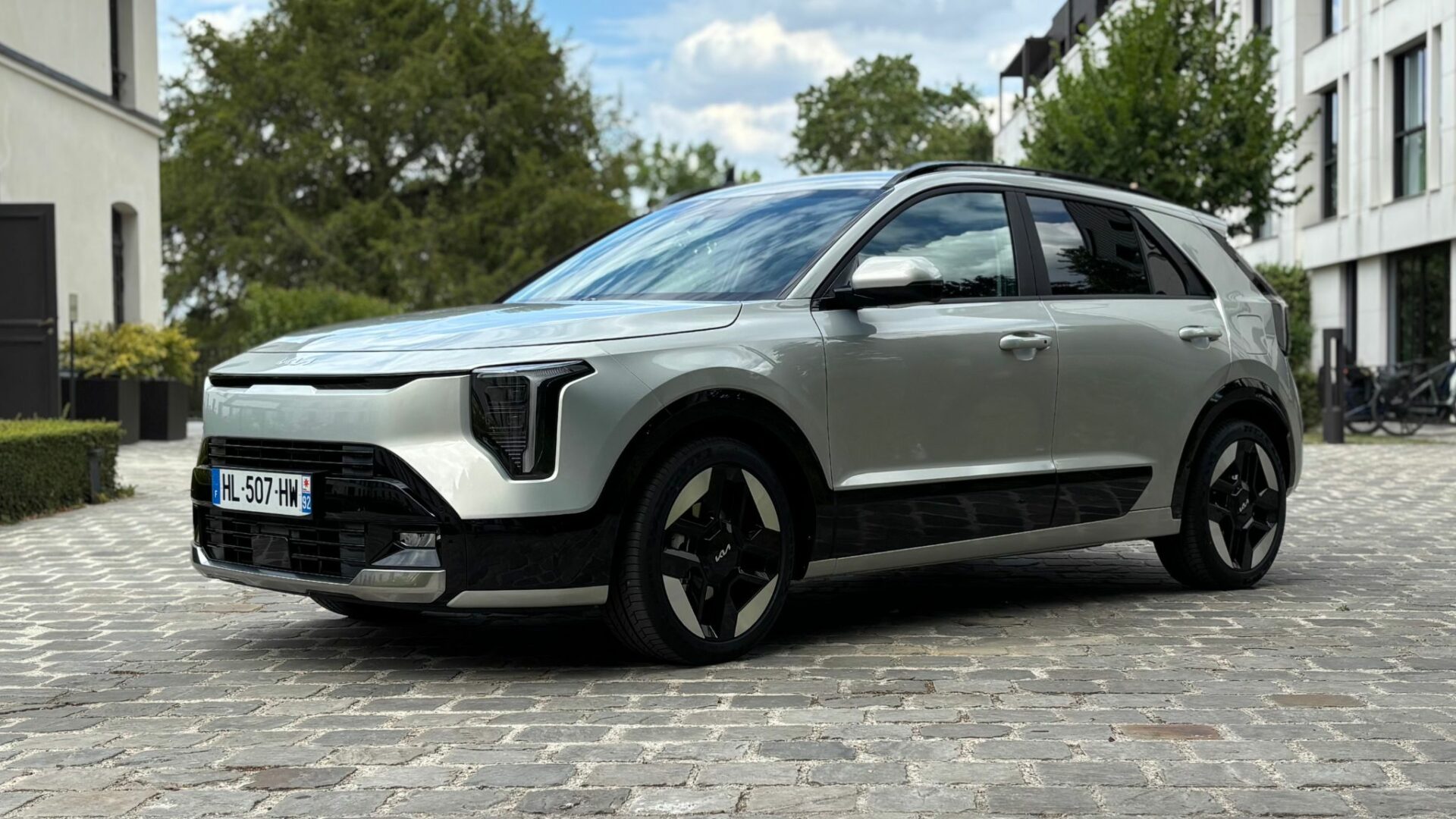 Kia Niro Hybride 2026 gris clair métallique de trois-quarts avant garé sur des pavés avec ses nouveaux phares verticaux