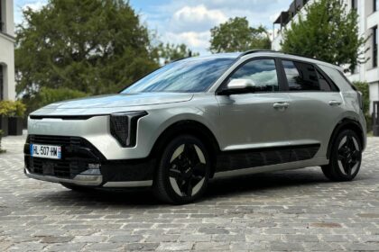 Kia Niro Hybride 2026 gris clair métallique de trois-quarts avant garé sur des pavés avec ses nouveaux phares verticaux