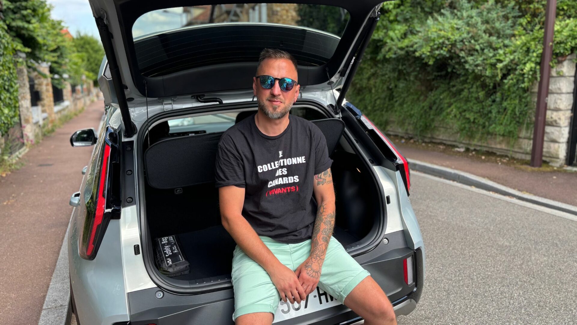 Victor Diakov assis confortablement dans le coffre du Kia Niro Hybride 2026 Gris Ivoire avec son t-shirt Ultra Vomit "Je collectionne des canards"