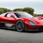 Vue de trois-quarts avant de la McLaren 6GT couleur rouge métallisé stationnée en bord de mer avec ses lignes néo-rétro