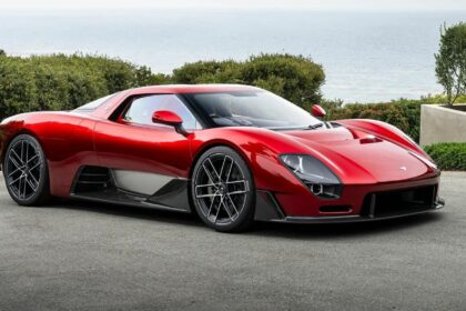 Vue de trois-quarts avant de la McLaren 6GT couleur rouge métallisé stationnée en bord de mer avec ses lignes néo-rétro