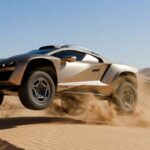 Le Rezvani Dune couleur bronze en plein saut au-dessus des dunes de sable dans le désert avec de la poussière sous les roues
