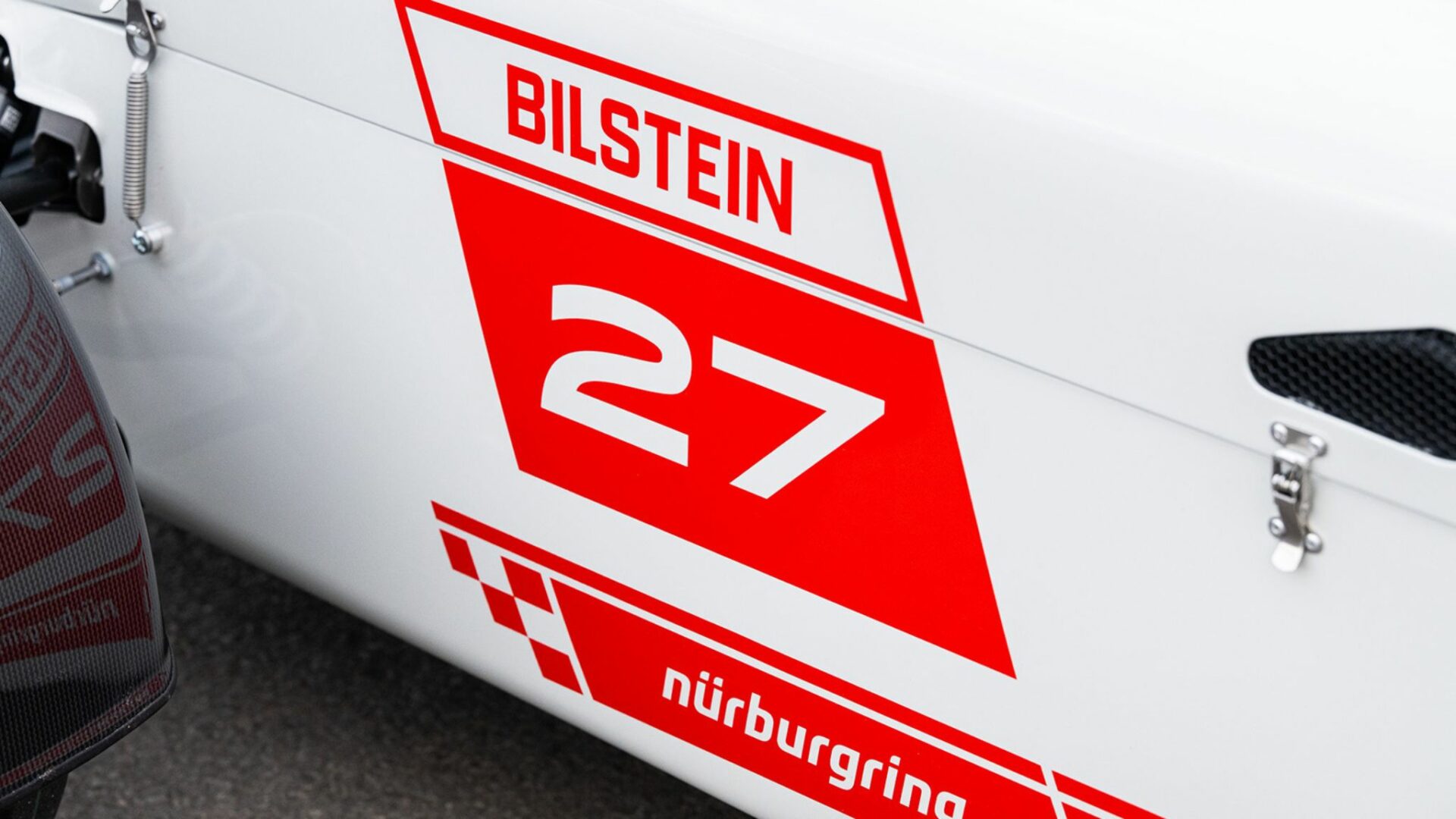 Détail du flanc latéral d'une Caterham Seven Nürburgring Edition blanche avec numéro 27, logo Bilstein et tracé du circuit