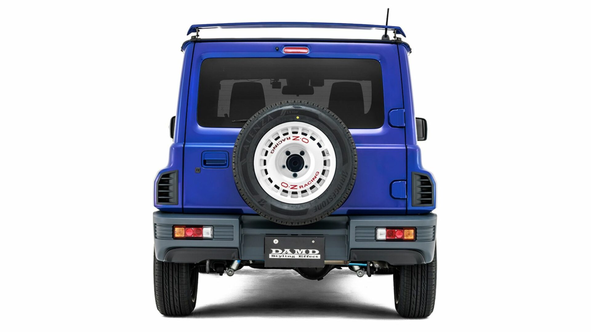 Vue arrière symétrique studio du Suzuki Jimny R5 DAMD bleu avec becquet de toit et roue de secours sur jante OZ Racing