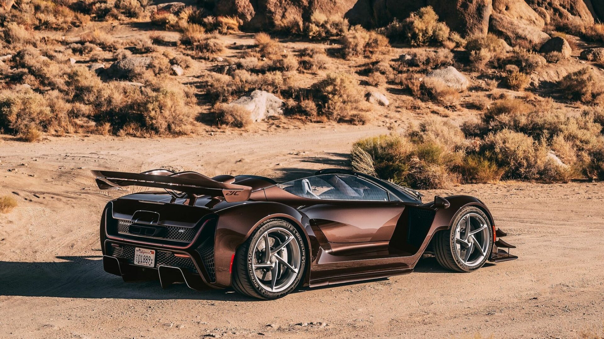 Vue de trois-quarts arrière de la Czinger 21C Spyder marron métallisée posée sur du sable dans un paysage désertique