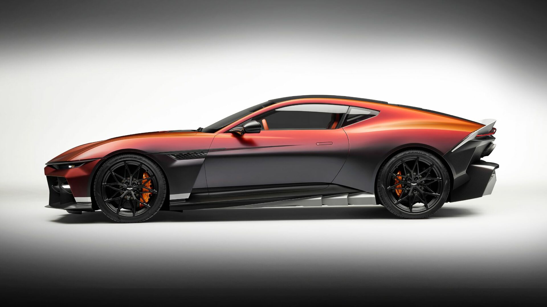 Vue de profil complet de l'Aston Martin Valen montrant sa garde au sol basse, son empattement, ses jantes noires et sa peinture dégradée