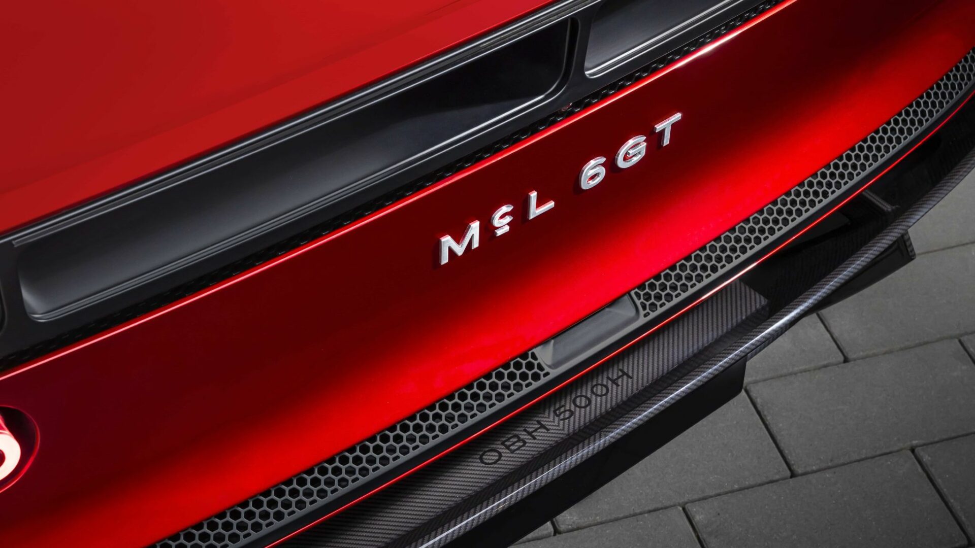 Gros plan sur le monogramme chromé MCL 6GT apposé sur la poupe rouge de la McLaren 6GT avec grille d'aération et diffuseur en carbone