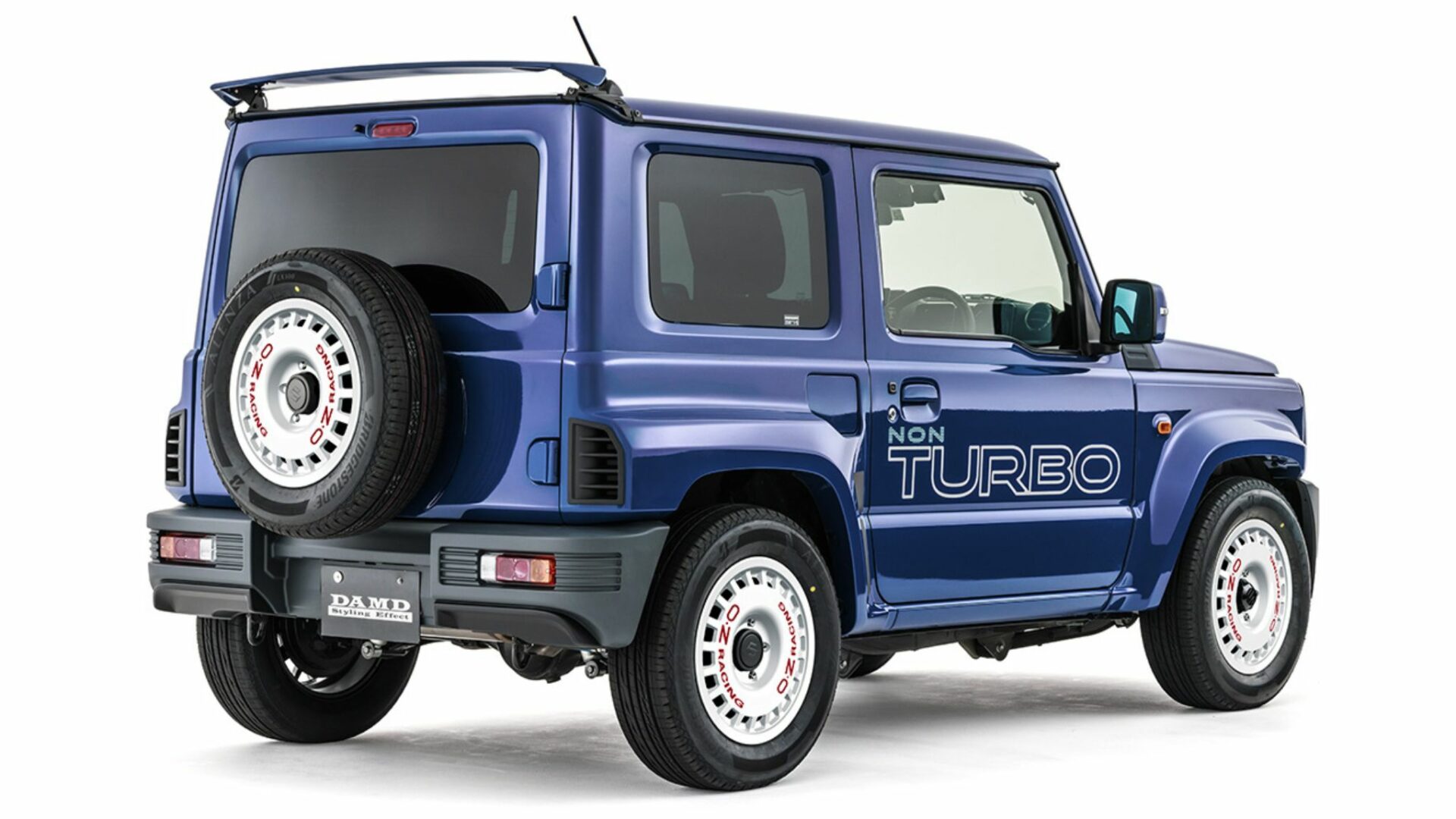 Vue trois-quarts arrière studio du Suzuki Jimny R5 DAMD avec béquet de toit, jantes blanches OZ Racing et sticker Non Turbo