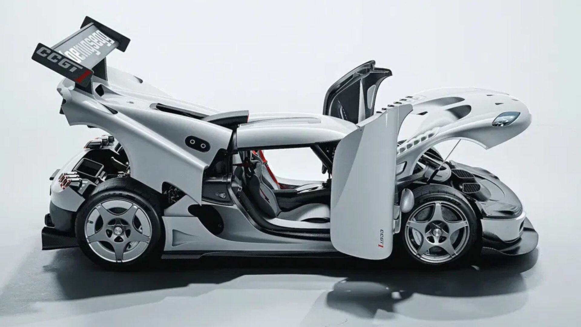 Vue de profil de la Koenigsegg CCGT1 sous éclairage studio avec le capot avant, le capot moteur arrière et les portes en dièdre grand ouverts