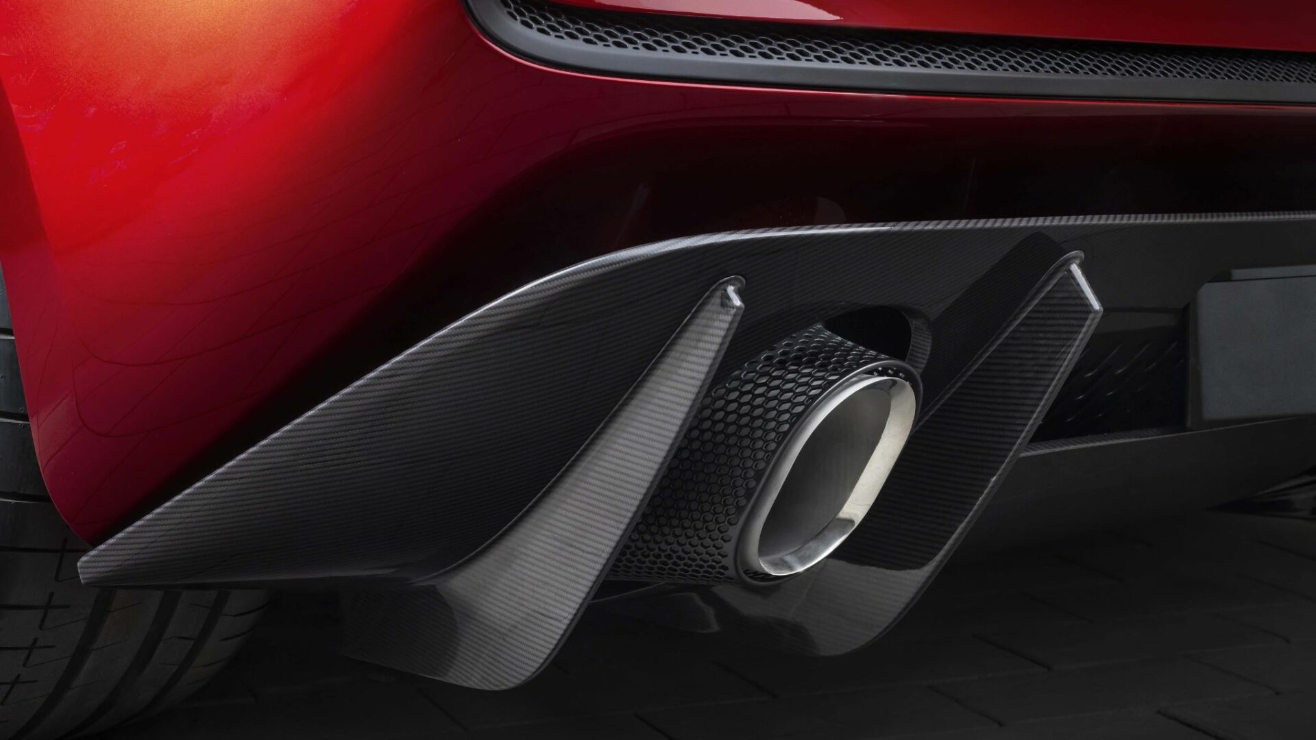 Gros plan sur la sortie d'échappement chromée et le massif diffuseur en fibre de carbone à l'arrière de la McLaren 6GT rouge