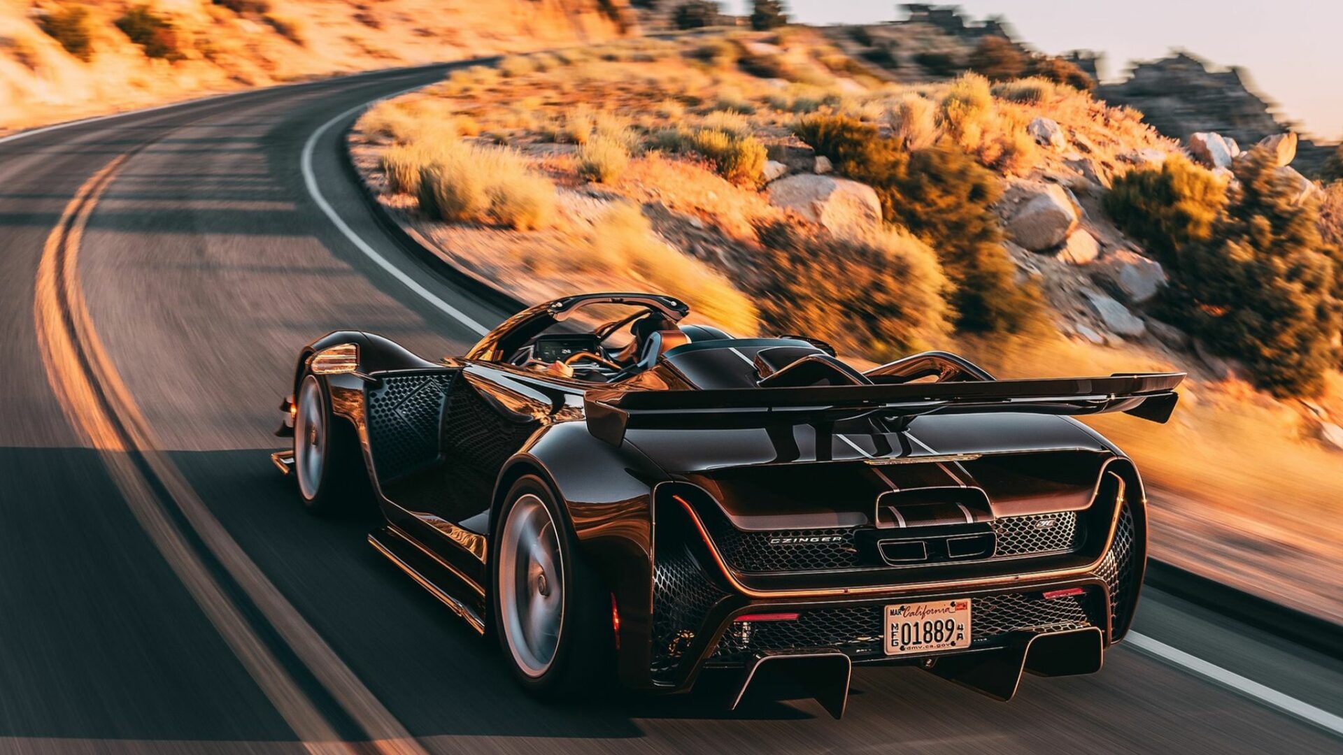 Vue de trois-quarts arrière en action de la Czinger 21C Spyder marron métallique négociant un virage sur une route sinueuse