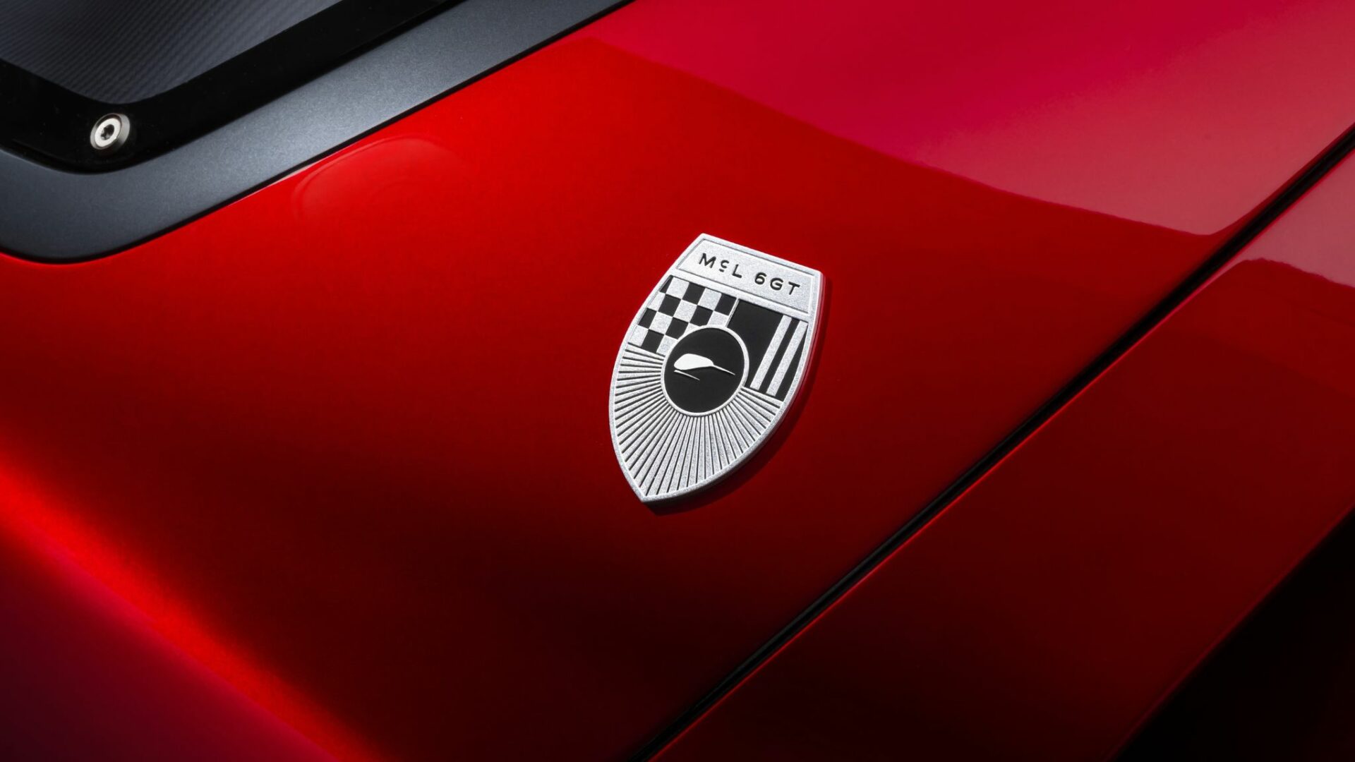 Gros plan sur l'écusson argenté et noir MCL 6GT fixé sur la carrosserie rouge métallisé de la McLaren 6GT