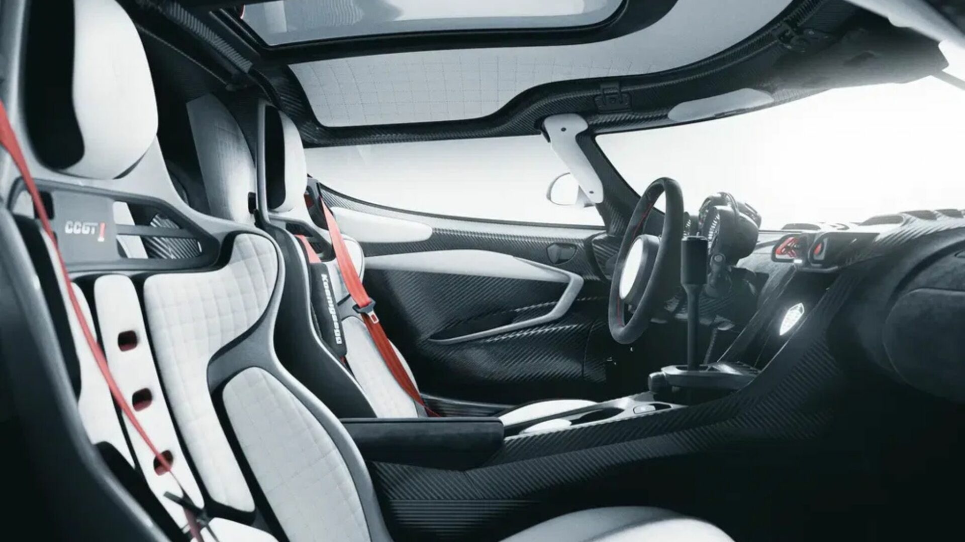 Vue de l'habitacle en fibre de carbone de la Koenigsegg CCGT1 montrant les sièges baquets blancs, le volant sport et le levier de vitesse KSS