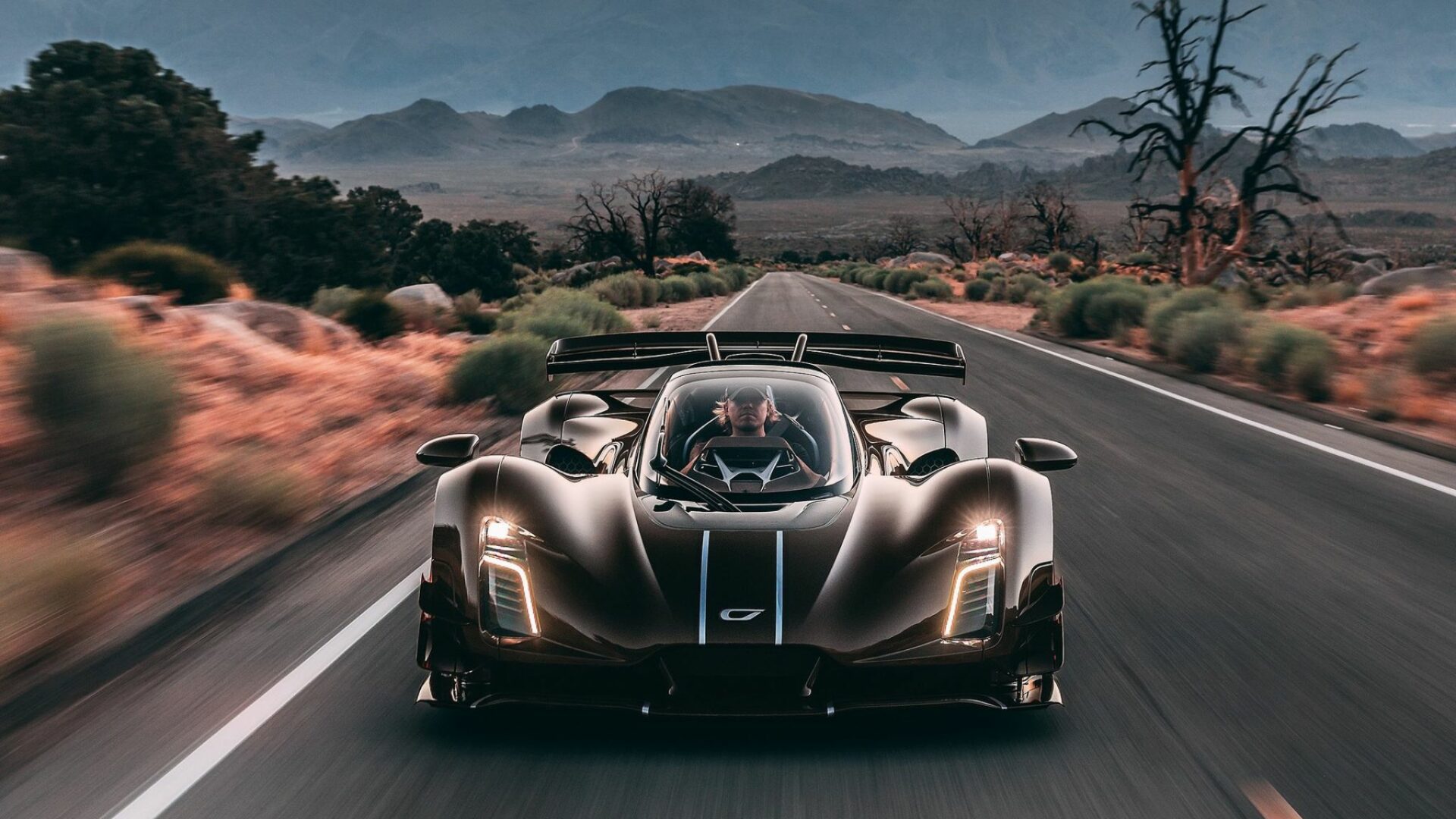Vue de face dynamique de l'hypercar Czinger 21C Spyder marron en pleine accélération sur une route désertique avec pilote visible au poste central