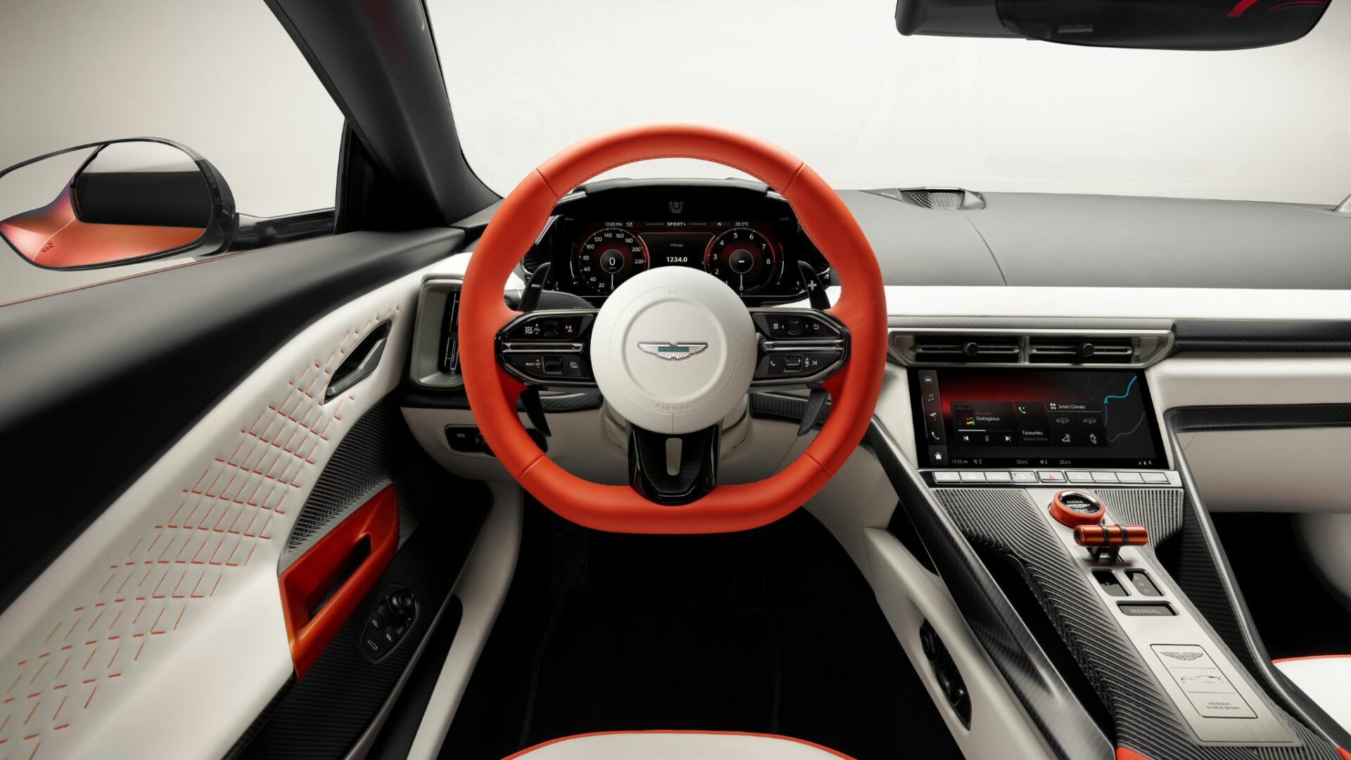 Vue d'ensemble du poste de pilotage de l'Aston Martin Valen avec son volant bicolore orange et blanc, ses compteurs numériques et sa console en carbone