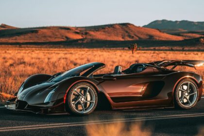 Vue de trois-quarts profil de la Czinger 21C Spyder marron métallique découvrable stationnée sur une route désertique au coucher du soleil