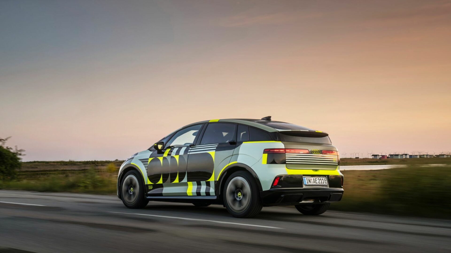 Audi A2 e-tron prototype camouflé avec stickers jaunes et noirs en plein roulage de trois-quarts arrière au coucher du soleil