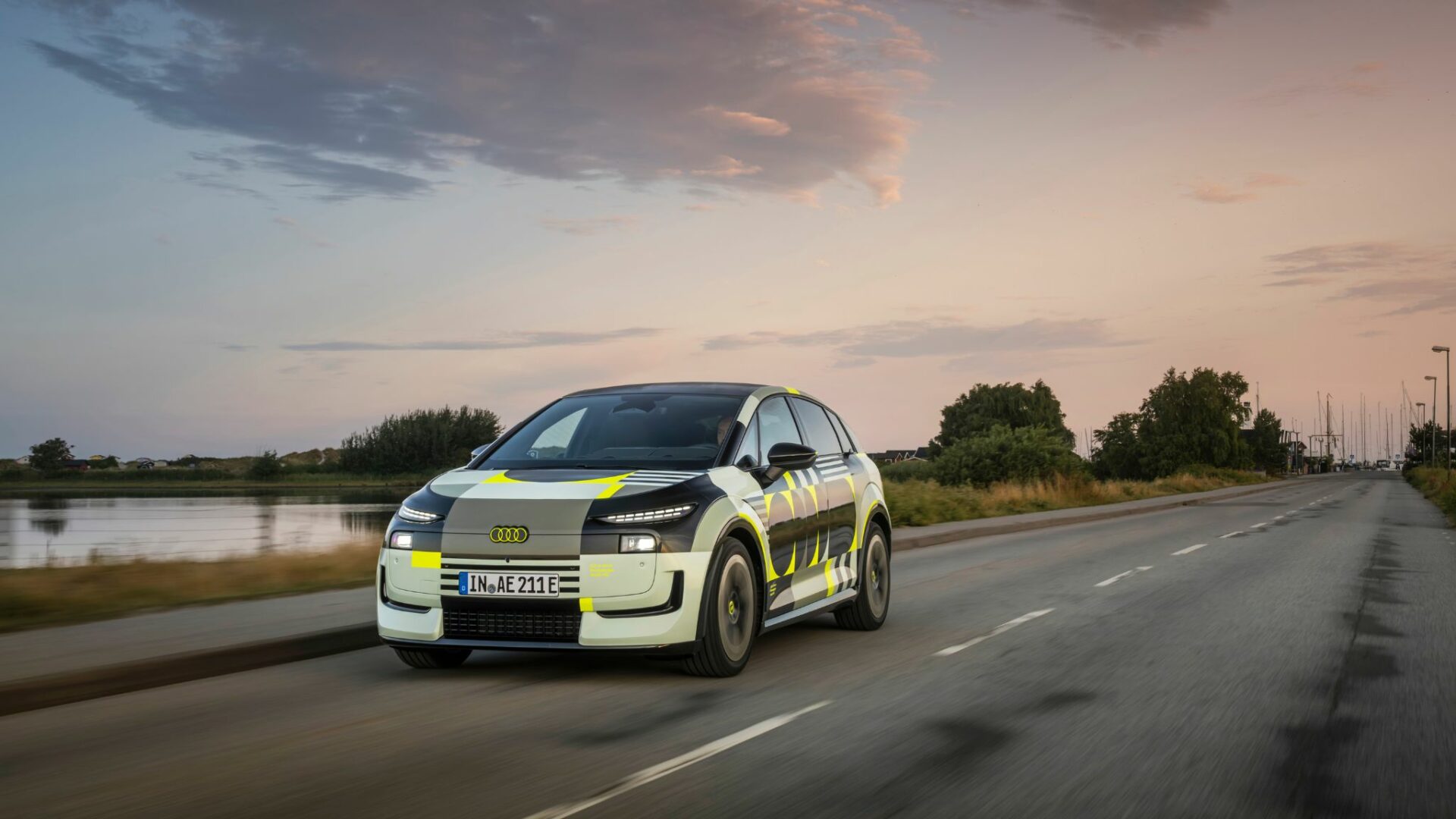 Audi A2 e-tron prototype camouflé avec détails jaune fluo en plein roulage de trois-quarts face au coucher du soleil