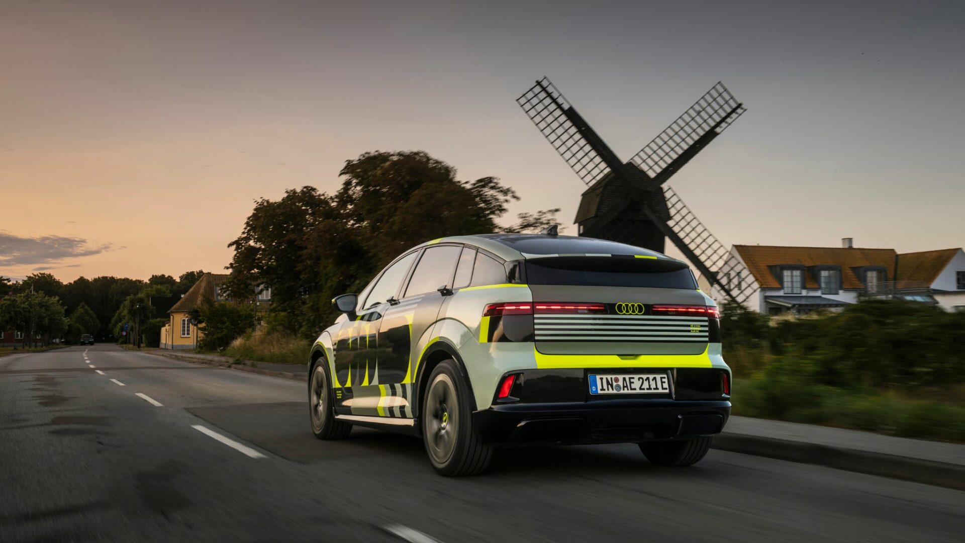 Audi A2 e-tron prototype camouflé en roulage de trois-quarts arrière sur route avec un moulin à vent traditionnel en arrière-plan