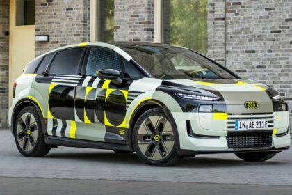 Audi A2 e-tron prototype camouflé stationné de trois-quarts face devant une façade en briques claires