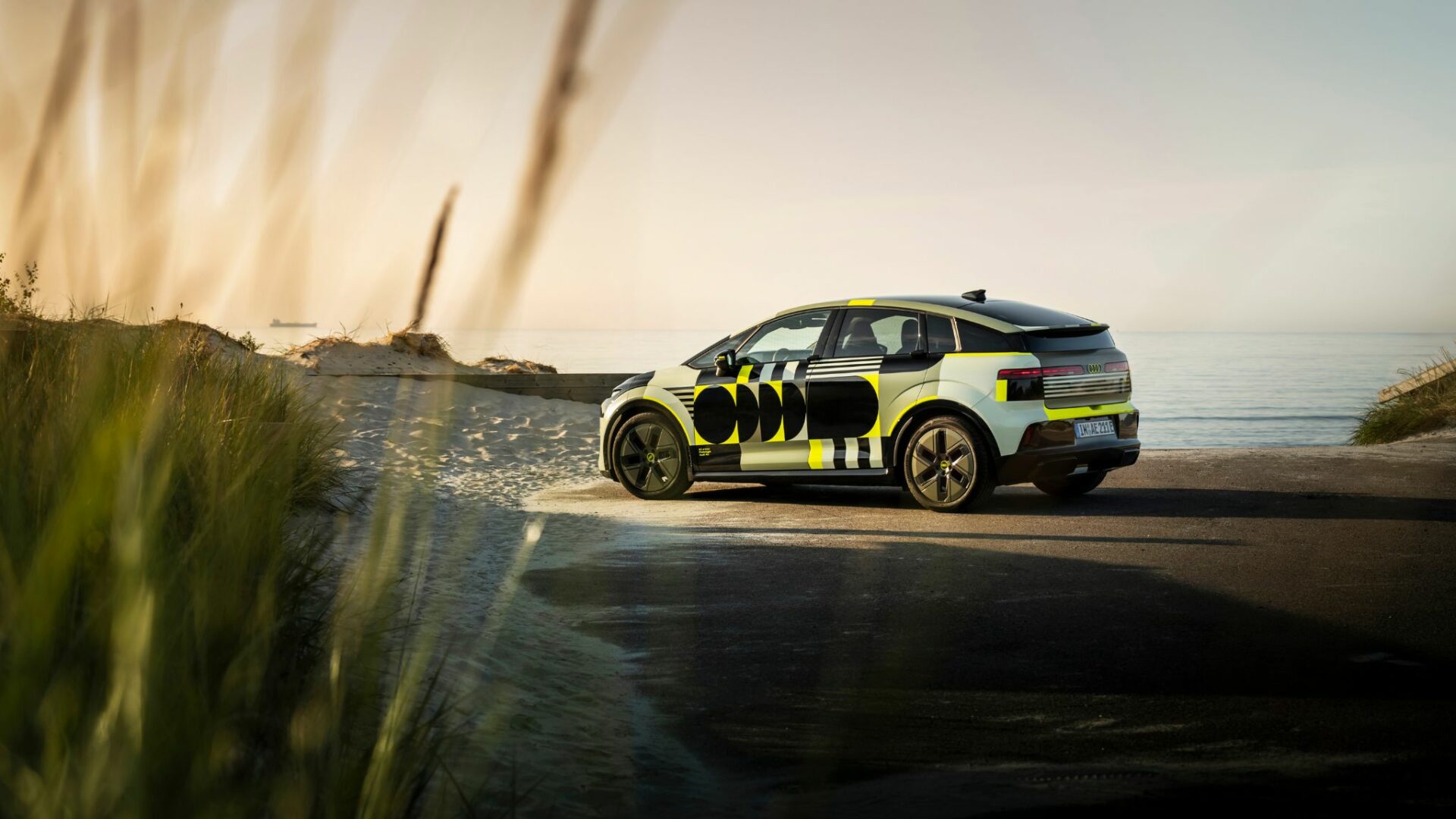 Vue latérale de l'Audi A2 e-tron prototype camouflé stationné au bord d'une plage près des dunes de sable sous une lumière dorée