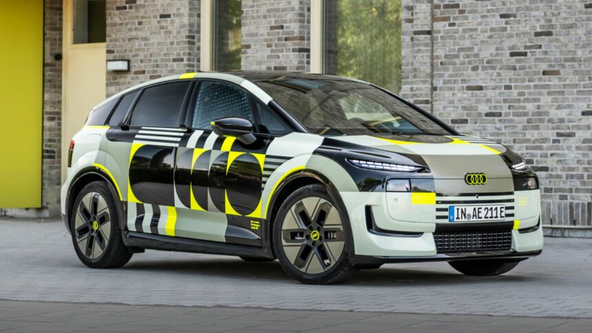 Audi A2 e-tron prototype camouflé stationné de trois-quarts face devant une façade en briques claires