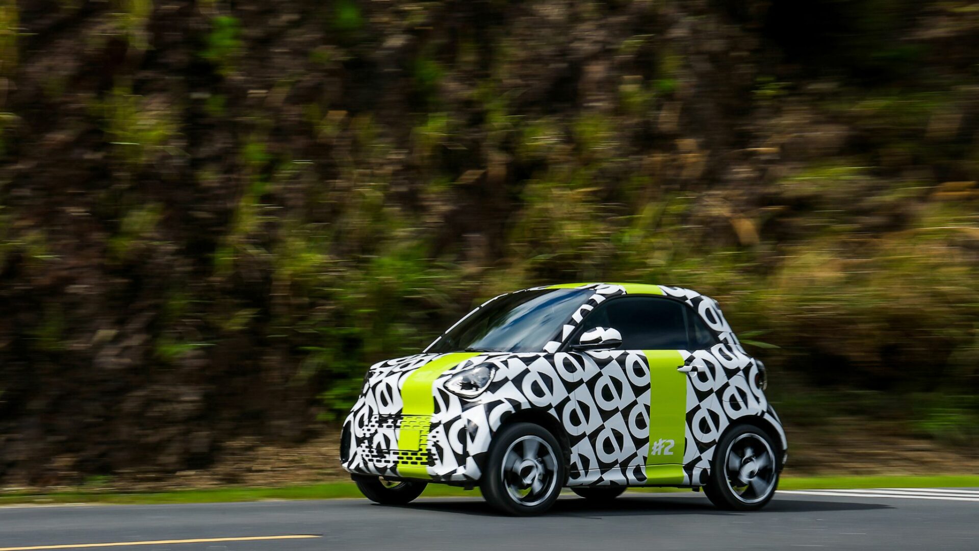Vue trois-quarts avant en mouvement du prototype camouflé de la Smart #2 en test de roulage dynamique sur route