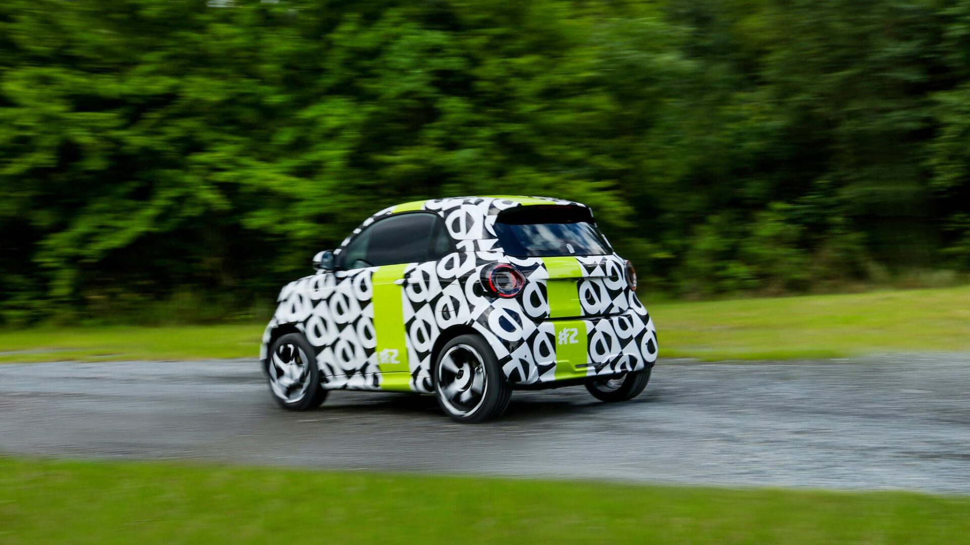 Vue trois-quarts arrière en mouvement du prototype camouflé de la Smart #2 en plein essai sur piste