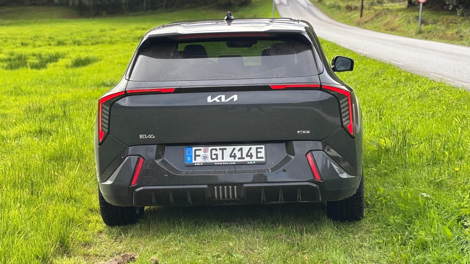 Vue arrière centrée de la nouvelle Kia EV4 GT grise stationnée sur herbe, mettant en valeur son bouclier arrière spécifique, ses feux LED et ses badges EV4 GT