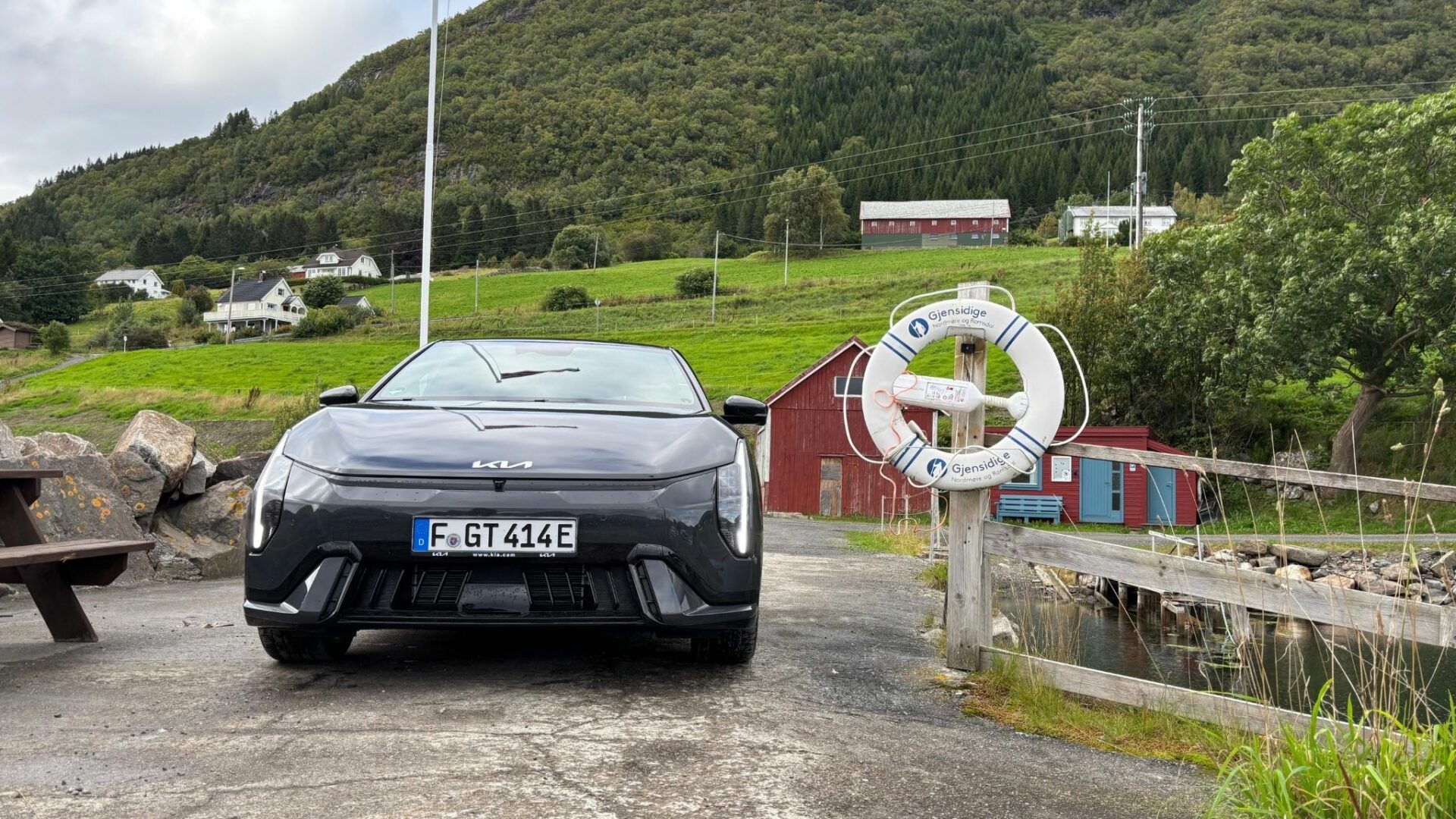Vue de face de la nouvelle Kia EV4 GT grise stationnée sur un quai au bord de l'eau près d'une bouée de sauvetage, dans un décor de village norvégien