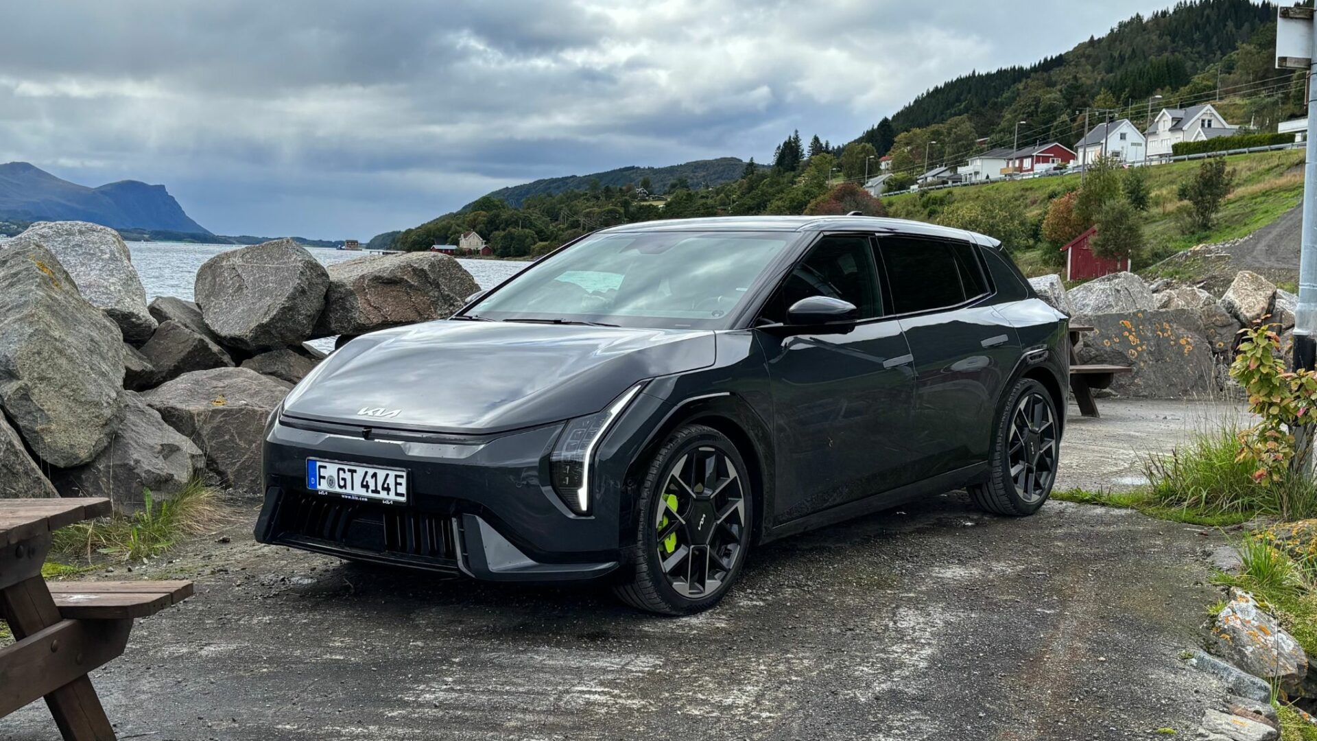 Vue de trois quarts avant de la nouvelle Kia EV4 GT grise garée sur un site côtier rocailleux face à un fjord et des montagnes en Norvège.