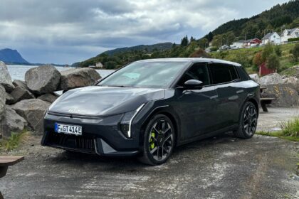 Vue de trois quarts avant de la nouvelle Kia EV4 GT grise garée sur un site côtier rocailleux face à un fjord et des montagnes en Norvège.