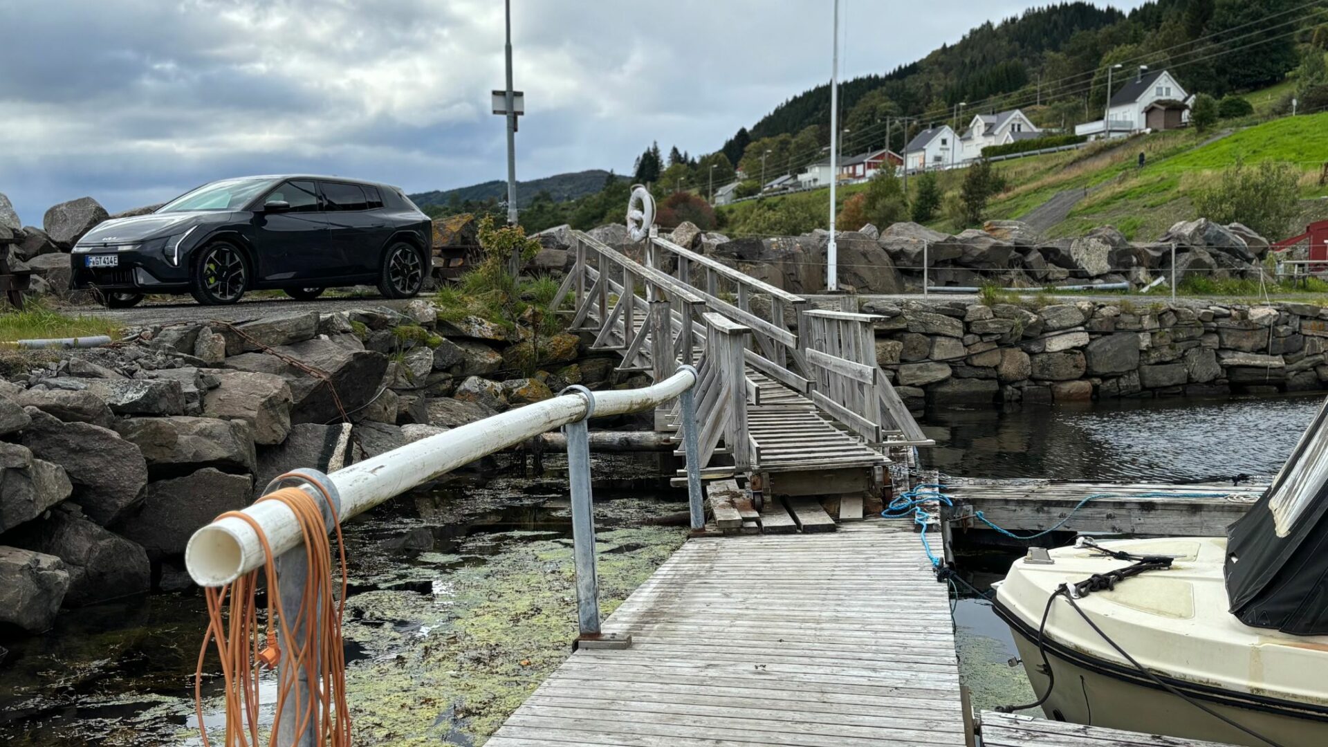 Vue d'ensemble de la nouvelle Kia EV4 GT grise garée sur un quai rocheux près d'une estacade en bois et d'un bateau dans un port norvégien.