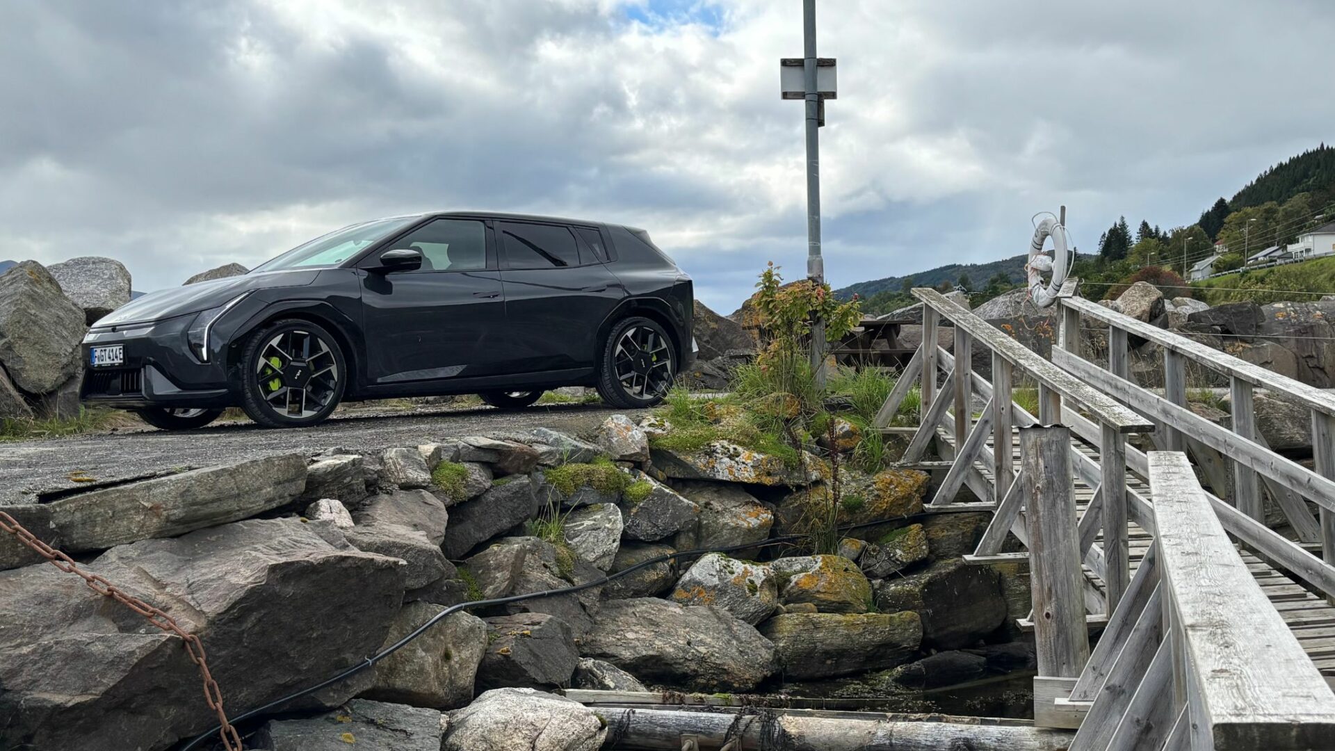 Vue de trois quarts avant de la nouvelle Kia EV4 GT grise stationnée sur un talus rocheux juste à côté d'un pont en bois dans un port de Norvège.