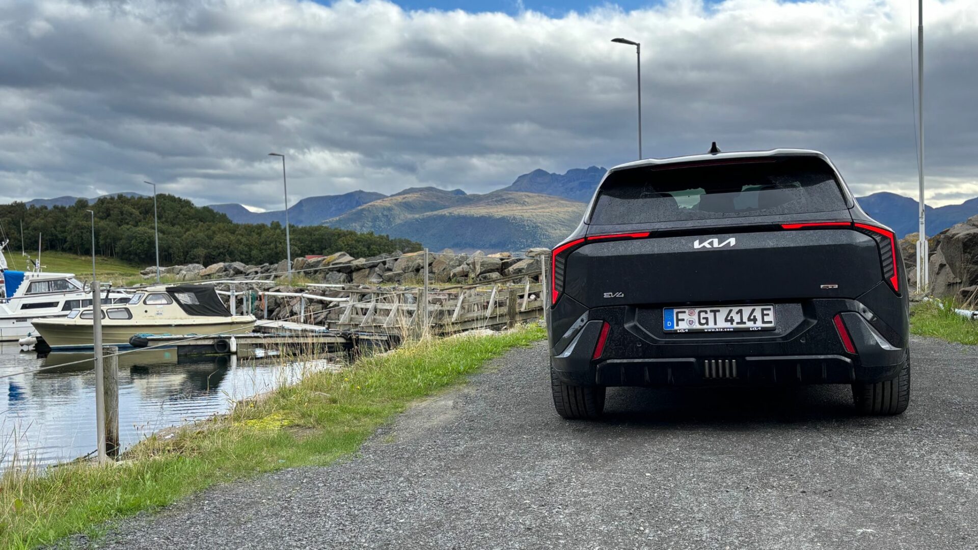 Vue arrière de la nouvelle Kia EV4 GT grise stationnée sur un chemin côtier longeant un port de plaisance et des bateaux, face aux montagnes en Norvège.