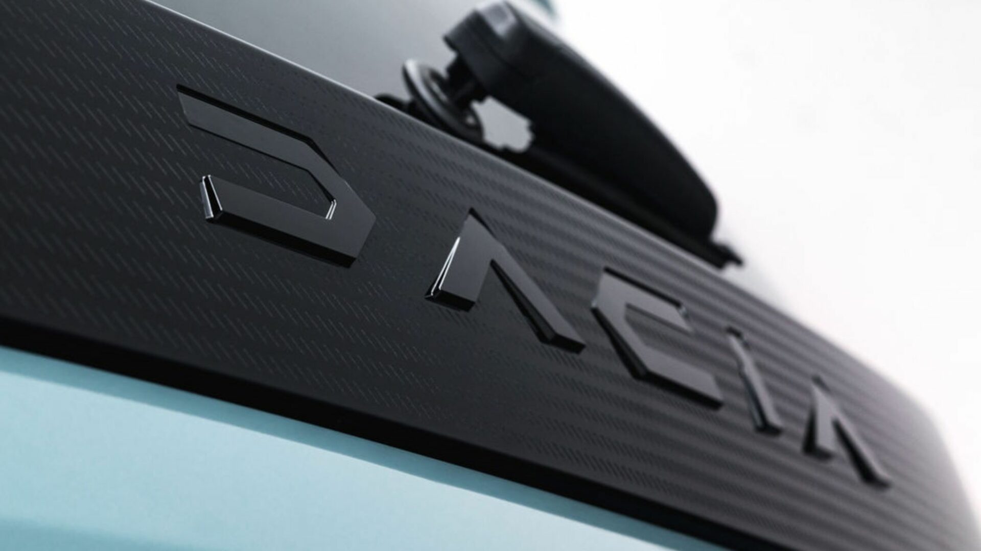 Gros plan sur le lettrage Dacia en relief intégré au bandeau noir texturé de la hayon de la Nouvelle Dacia Spring.