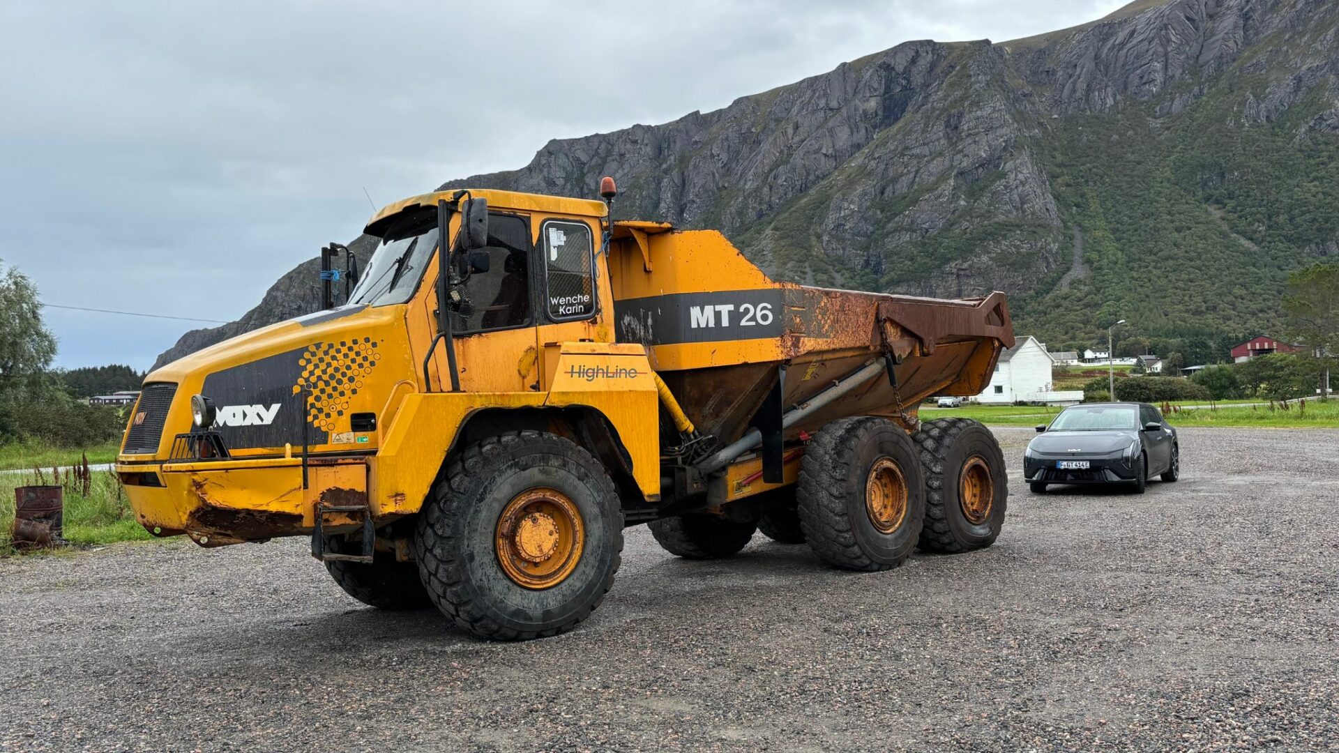 Vue d'ensemble de la nouvelle Kia EV4 GT grise stationnée en arrière-plan d'un énorme camion de chantier jaune Moxy MT 26 dans les paysages norvégiens.