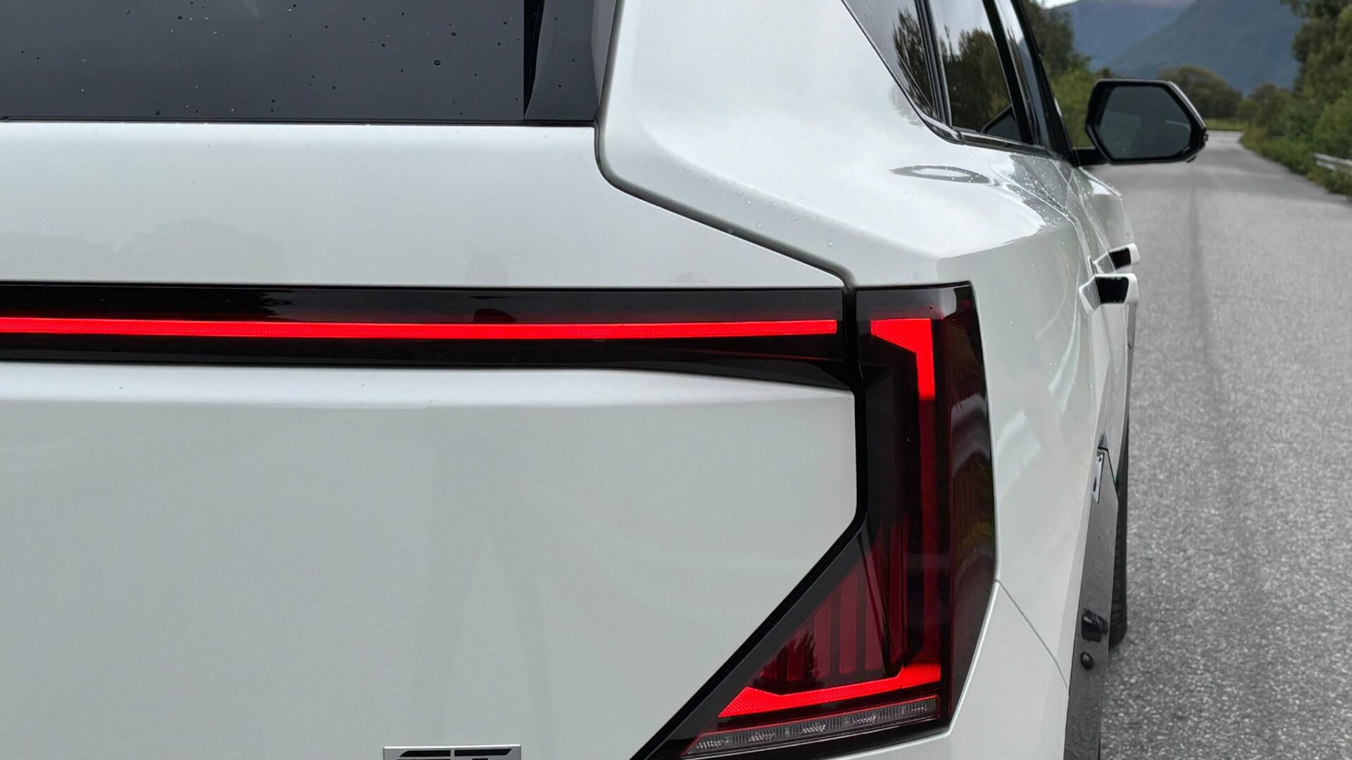 Gros plan sur le bloc optique arrière à LED et le bandeau lumineux de la nouvelle Kia EV5 GT blanche lors des essais sur route.