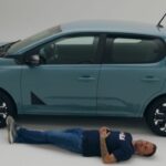 Le youtubeur automobile Victor Diakov allongé le long de la Nouvelle Dacia Spring pour illustrer le gabarit de la citadine électrique.