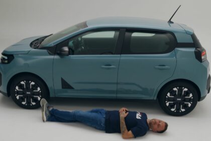 Le youtubeur automobile Victor Diakov allongé le long de la Nouvelle Dacia Spring pour illustrer le gabarit de la citadine électrique.