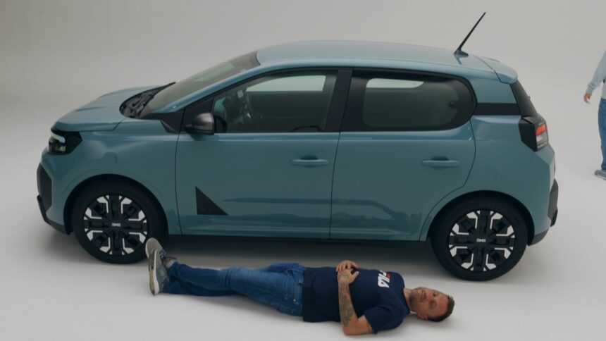 Le youtubeur automobile Victor Diakov allongé le long de la Nouvelle Dacia Spring pour illustrer le gabarit de la citadine électrique.