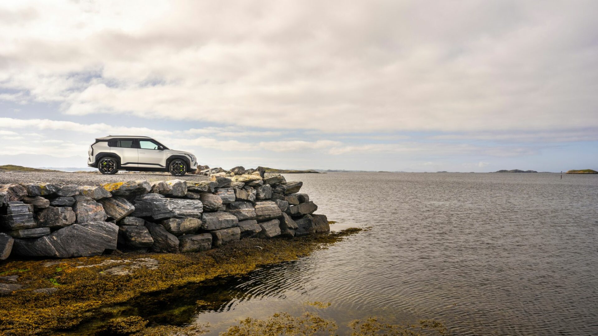 La nouvelle Kia EV3 GT stationnée au bord de l'eau sur un muret de pierres dans les paysages nordiques, mettant en valeur son design de SUV compact sportif.