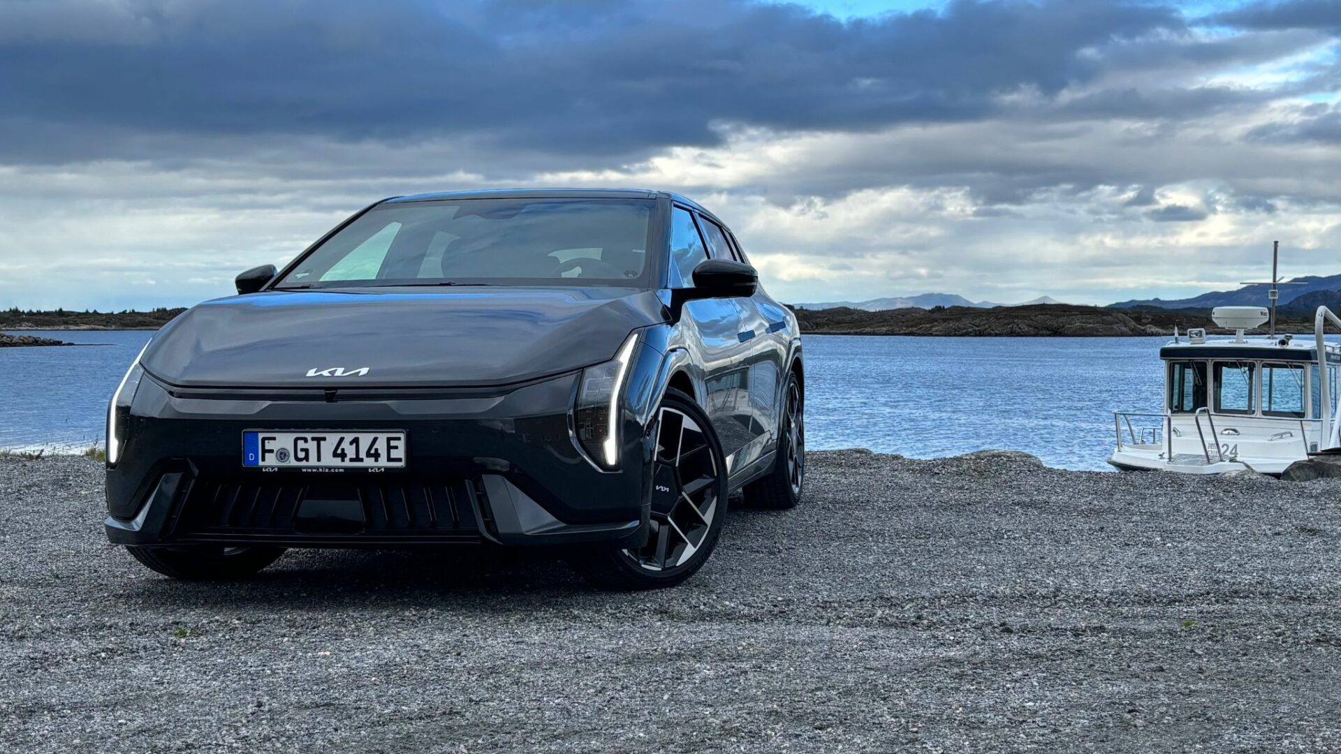 Vue de face de la nouvelle Kia EV4 GT grise stationnée au bord d'un plan d'eau en Norvège, mettant en valeur son bouclier agressif et sa signature lumineuse à LED.