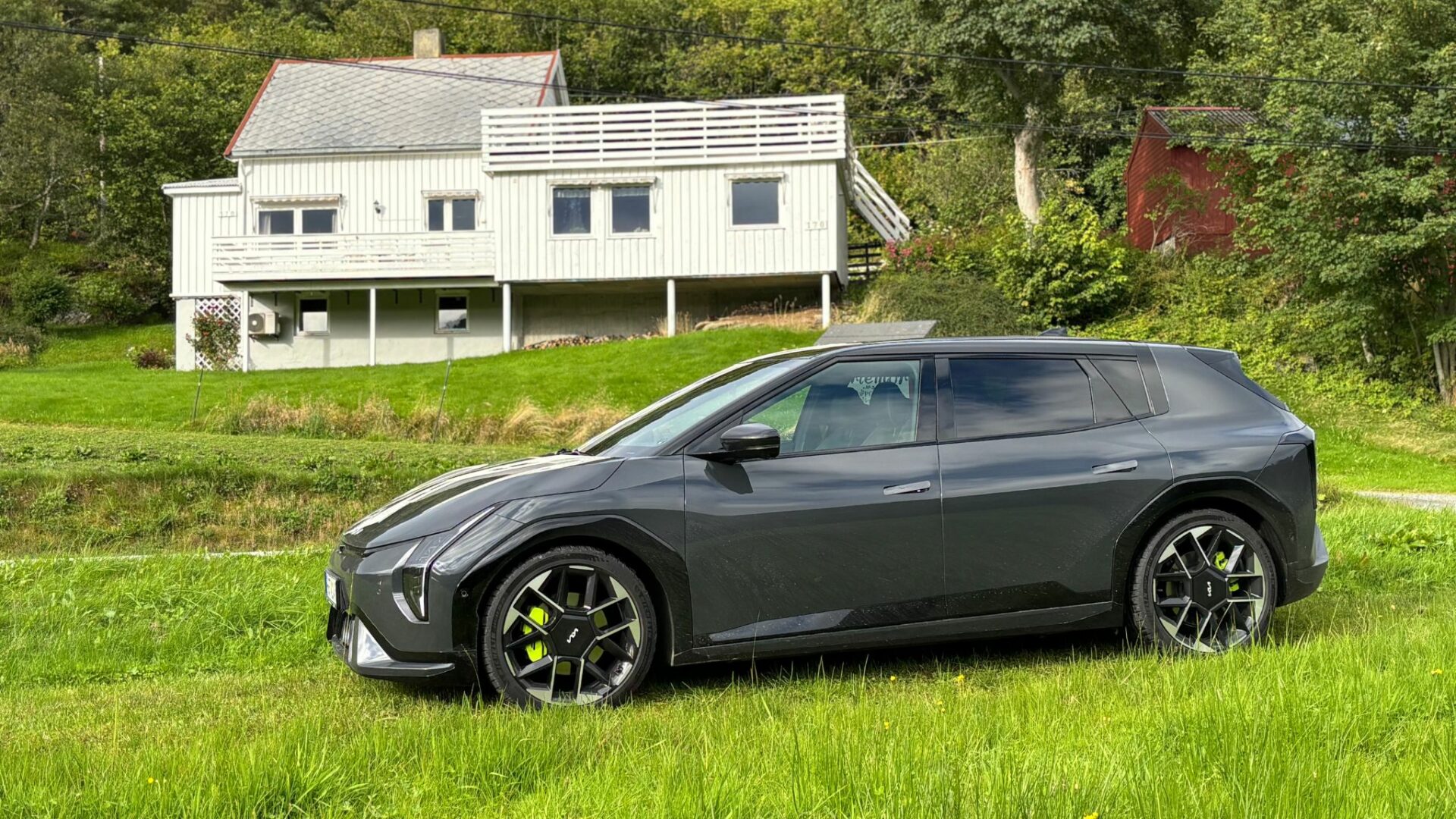 Vue de profil de la nouvelle Kia EV4 GT grise garée sur une pelouse verdoyante devant une maison blanche traditionnelle en Norvège.