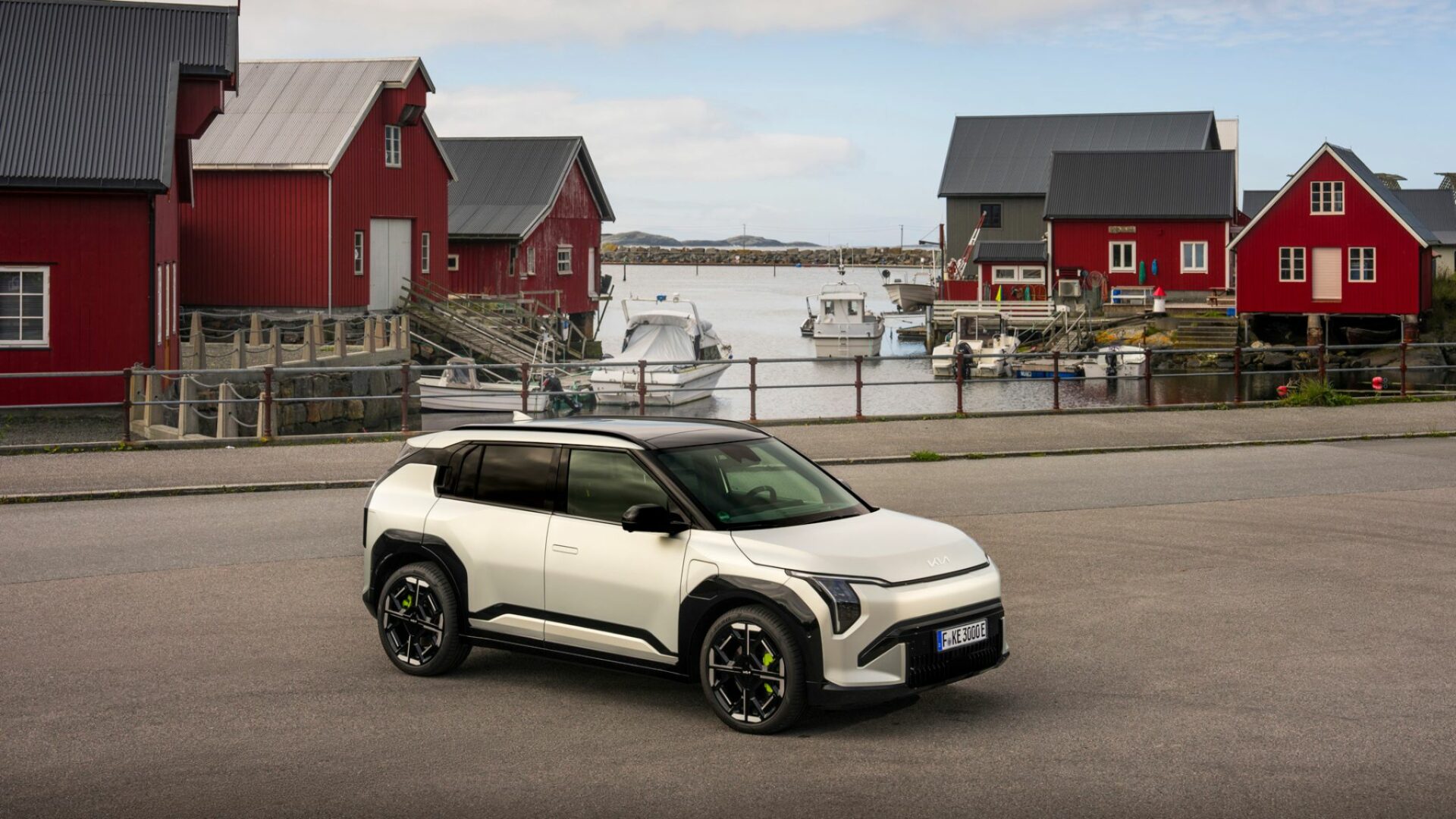 Vue aérienne de trois quarts avant de la Kia EV3 GT garée sur un port devant des cabanes rouges traditionnelles en Norvège, mettant en valeur son design de SUV compact sportif.